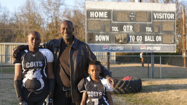 This photo provided by the University of Maryland shows Ronald Redmond standing with sons, 11-year-old R.J., left, and 7-year-old Mason on a football field in Lexington, Mississippi, Jan. 4, 2024. Lexington, Miss. is located in the second-poorest county in the nation’s poorest state. Yet a new analysis shows the town sends more players per capita to elite college football programs than any other town in Mississippi – at a rate that’s among the top in the nation. For many families, the game offers hope for college and a future. (University of Maryland/Jenna Bloom via AP)