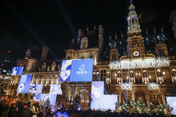 People watch the Paris city hall with its new decoration inspired by the Paris2024 Olympic Games, Tuesday, Nov. 28, 2023 in Paris. (AP Photo/Thomas Padilla)