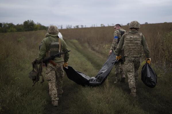 Ukrainian servicemen carry a bag containing the body of a Ukrainian soldier, center, as one of them, right, carries the remains of a body of a Russian soldier in a retaken area near the border with Russia in Kharkiv region, Ukraine, Saturday, Sept. 17, 2022. (AP Photo/Leo Correa)