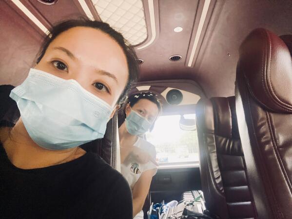 In this image provided by Joys Tan, graphic designer Tan, left, takes a selfie with her friend while onboard a bus that will take them to their quarantine hotel in Singapore on Sept. 21, 2021. As the island nation of Singapore pursues a strategy of "living with COVID" and a gradual relaxation of pandemic restrictions, daily cases are skyrocketing and residents are growing increasingly anxious. (Joys Tan via AP)