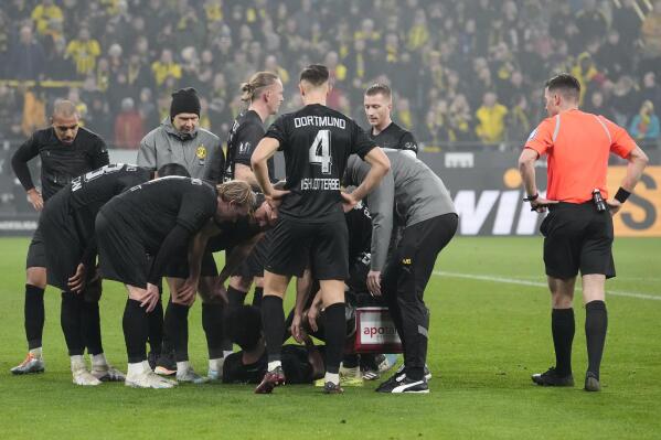 Dortmund's Karim Adeyemi, center, surrounded by support staff and teammates lies injured on the pitch during the German Bundesliga soccer match between Borussia Dortmund and Hertha BSC Berlin in Dortmund, Germany, Sunday, Feb. 19, 2023. (AP Photo/Martin Meissner)
