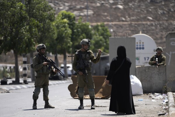 FILE - Israeli soldiers speak to a Palestinian woman near the site of an alleged car-ramming attack near Beit Hagai, a Jewish settlement in the hills south of the large Palestinian city of Hebron, Wednesday, Aug. 30, 2023. The United Nations' highest court opens historic hearings Monday, Feb. 19, 2024, into the legality of Israel's 57-year occupation of the West Bank and east Jerusalem, plunging the 15 international judges back into the heart of the decades-long Israeli-Palestinian conflict. (APPhoto/Mahmoud Illean, File)