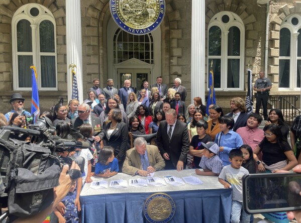 Nevada Gov. Joe Lombardo signs a bill to provide more rural and tribal school funding, flanked by dozens of legislators, tribal members and students outside the state Capitol building on Tuesday, June 13, 2023, in Carson City, Nev. The new legislation also funds a new Owyhee Combined School School on the Duck Valley Indian Reservation along the Nevada-Idaho border. (AP Photo/Gabe Stern)