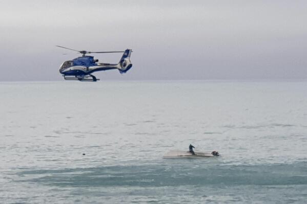 A helicopter flies overs an upturned boat with a survivor sitting on the hull off the coast of Kaikoura, New Zealand, Saturday, Sept. 10, 2022. A boat in New Zealand collided with a whale and capsized. (AP Photo)
