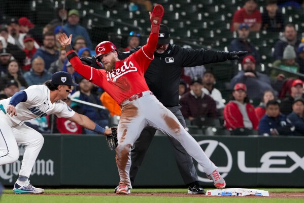 Cincinnati Reds' Jake Fraley is originally called safe stealing third base by umpire Rob Drake in front of the tag from Seattle Mariners third baseman Josh Rojas, left, during the fourth inning of a baseball game Monday, April 15, 2024, in Seattle. Fraley lost his balance and was then called out. (AP Photo/Lindsey Wasson)