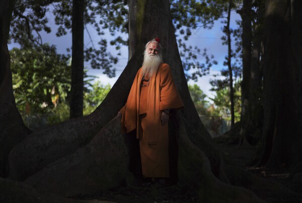 Paramacharya Sadasivanatha Palaniswami stands at the base of a Rudraksha tree, which produces a bright blue fruit at the Kauai Hindu Monastery on July 10, 2023, in Kapaa, Hawaii. The monks who reside at the temple monastery practice Shaivism, one of the major Hindu traditions, which worships Shiva as the supreme being. (AP Photo/Jessie Wardarski)