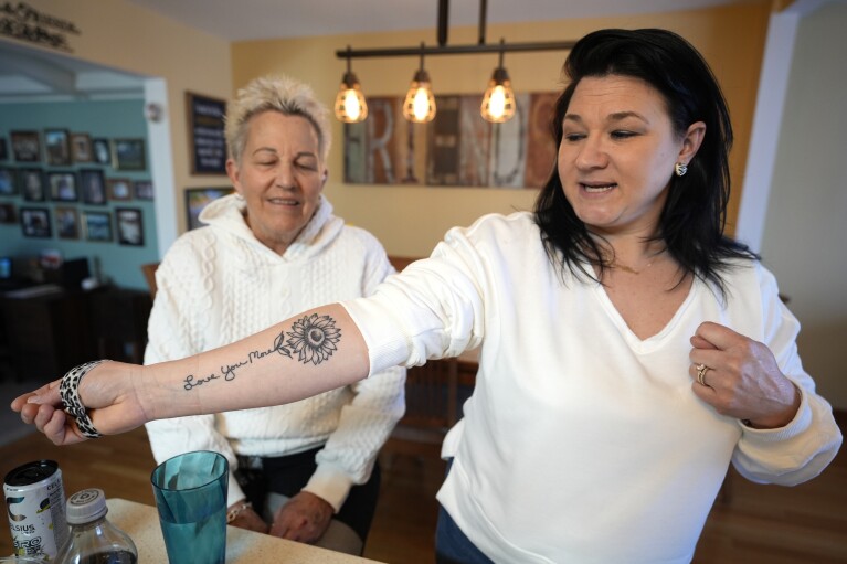 Shannon Rodriguez, right, shows off a tattoo made of her mother Deb Robertson's handwriting "Love You More" and sunflower at Robertson's Lombard, Ill., home Saturday, March 23, 2024. Robertson didn’t cry when she learned two months ago that the cancerous tumors in her liver were spreading, portending a tormented death. But later, she cried after receiving a call that a bill moving through the Illinois Legislature to allow certain terminally ill patients to end their own lives with a doctor’s help had made progress. (AP Photo/Charles Rex Arbogast)