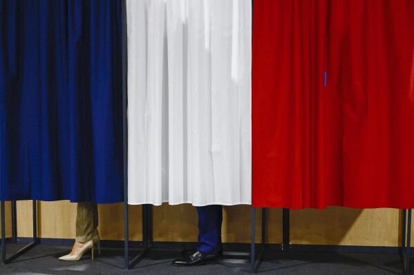 French President Emmanuel Macron and his wife Brigitte Macron stand in the voting booth before voting in Le Touquet-Paris-Plage, northern France, Sunday, June 30, 2024. (Yara Nardi, Pool via AP)
