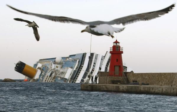 FILE— Seagulls fly in front of the grounded cruise ship Costa Concordia off the Tuscan island of Isola del Giglio, Italy, Monday, Jan. 30, 2012. Italy on Thursday, Jan. 13, 2022, is marking the 10th anniversary of the Concordia disaster with a daylong commemoration, honoring the 32 people who died but also the extraordinary response by the residents of Giglio who took in the 4,200 passengers and crew from the ship on that rainy Friday night and then lived with the Concordia carcass for another two years before it was hauled away for scrap. (AP Photo/Pier Paolo Cito)