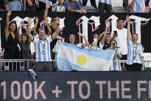 Fans wave an Argentinian flag as they try to get Inter Miami forward Lionel Messi's attention as he warms up before the start of an MLS soccer match between Inter Miami and Toronto FC, Wednesday, Sept. 20, 2023, in Fort Lauderdale, Fla. It's almost necessary to be an A-lister to score a ticket to watch him play: A front-row ticket for an upcoming match between Inter Miami and the Chicago Fire at Soldier Field was going for $2,500.(AP Photo/Wilfredo Lee)