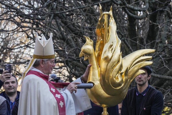 Paris Archbishop Laurent Ulrich places the relics of a fragment of Christ's crown of thorns and remains of St. Denis and St. Genevieve into the replica of the golden rooster before being craned up to the top of the spire as part of restoration works of Notre Dame Cathedral Saturday, Dec. 16, 2023. Notre Dame Cathedral got its rooster back Saturday, in a pivotal moment for the Paris landmark's restoration following the devastating fire in April 2019. (AP Photo/Michel Euler)