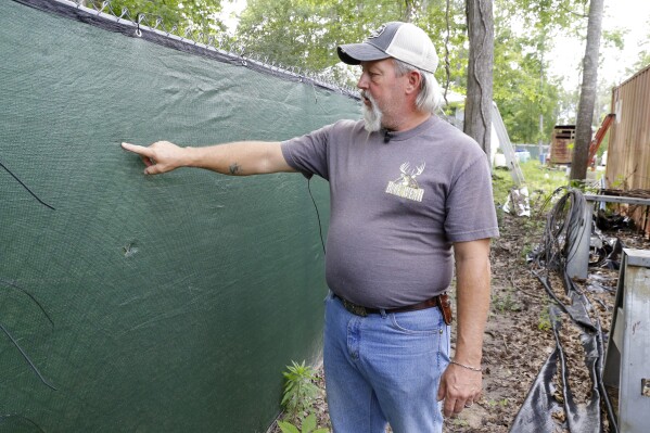 Keith Pinkson points out bullet holes in his fence as he explains how his daughter was nearly hit by gunfire from a neighbor's handgun earlier in the year, during an interview Tuesday, May 16, 2023, at his home in San Jacinto County, Texas. Pinkston called the San Jacinto County Sheriff's office, but Pinkston says they did nothing after arriving - not even checking the ID of anyone involved in the call. It was later discovered the neighbor was a convicted sex offender who should not have a weapon, which could have been determined with a simple ID check. (AP Photo/Michael Wyke)