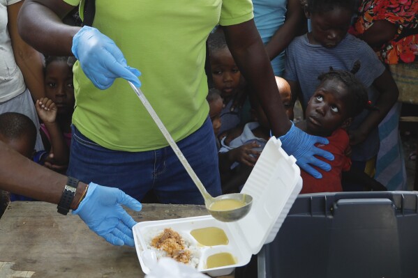 A server ladles soup into a container as children line up to receive food at a shelter for families displaced by gang violence, in Port-au-Prince, Haiti, Thursday, March 14, 2024. (AP Photo/Odelyn Joseph)