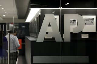 FILE - In this April 18, 2017, file photo, people walk by Associated Press photographs on display at The AP headquarters in New York. The Associated Press changed its influential style guide Friday, June 19, 2020, to capitalize the “b” in the term Black when referring to people, weighing in on a hotly debated issue. (AP Photo/Jenny Kane, File)
