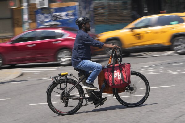 FILE - A delivery worker rides a motorized bicycle, July 25, 2023, in New York. On Monday, Nov. 13, New York City officials said that retailers and food delivery companies must do more to halt the proliferation of unsafe e-bike and e-scooter batteries after a fire blamed on an electric scooter's lithium ion battery killed three people over the weekend. (AP Photo/Seth Wenig, File)