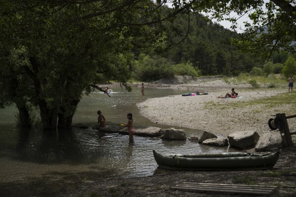 Visitors bathe in the the Lac de Castillon, southern France, Tuesday, June 24, 2023. Human-caused climate change is lengthening droughts in southern France, meaning the reservoirs are increasingly drained to lower levels to maintain the power generation and water supply needed for nearby towns and cities. (AP Photo/Daniel Cole)