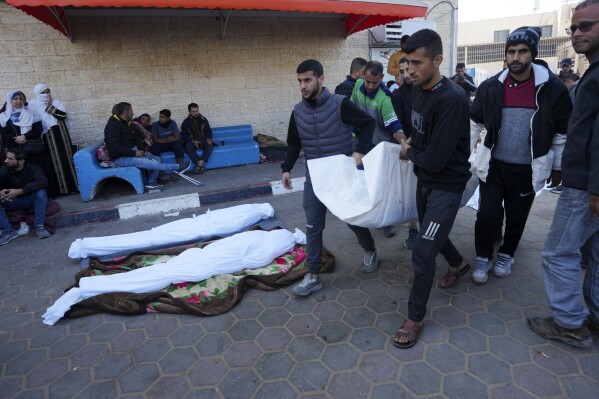 Palestinians carry a relative killed in the Israeli bombardment of the Gaza Strip, in front of the morgue at the hospital in Deir al Balah, Gaza Strip, Monday, Dec. 18, 2023. (AP Photo/Adel Hana)