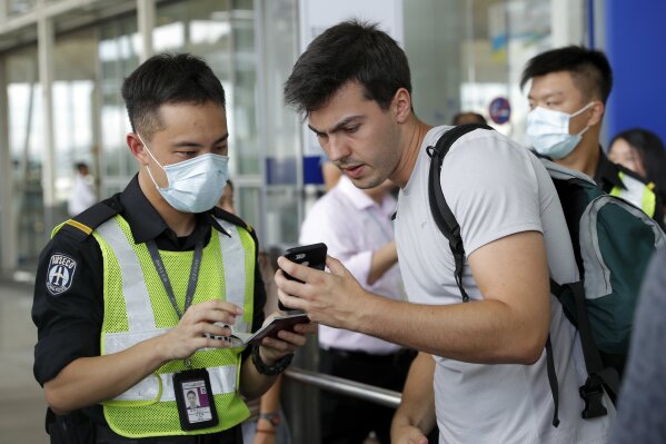 An airport security officer checks on a traveller's flight information at the airport main entrance gate in Hong Kong, Wednesday, Aug. 14, 2019. Flights resumed at Hong Kong's airport Wednesday morning after two days of disruptions marked by outbursts of violence that highlight the hardening positions of pro-democracy protesters and the authorities in the semi-autonomous Chinese city. (AP Photo/Vincent Thian)