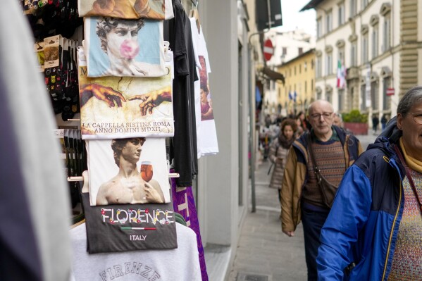 People walk past a shop selling souvenirs of Michelangelo's 16th century statue of David, in downtown Florence, central Italy, Monday, March 18, 2024. Michelangelo’s David has been a towering figure in Italian culture since its completion in 1504. But curators worry the marble statue’s religious and political significance is being diminished by the thousands of refrigerator magnets and other souvenirs focusing on David’s genitalia. The Galleria dell’Accademia’s director has positioned herself as David’s defender and takes swift aim at those profiteering from his image. (AP Photo/Andrew Medichini)