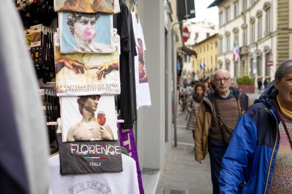 People walk past a shop selling souvenirs of Michelangelo's 16th century statue of David, in downtown Florence, central Italy, Monday, March 18, 2024. Michelangelos David has been a towering figure in Italian culture since its completion in 1504. But curators worry the marble statues religious and political significance is being diminished by the thousands of refrigerator magnets and other souvenirs focusing on Davids genitalia. The Galleria dellAccademias director has positioned herself as Davids defender and takes swift aim at those profiteering from his image. (AP Photo/Andrew Medichini)
