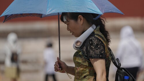 FILE - A woman wearing an electric fan and carrying an umbrella visits the Forbidden City on a sweltering day in Beijing, on July 7, 2023. Earlier this week, Beijing reported more than nine straight days with temperatures above 35 degrees Celsius (95 degrees Fahrenheit), a streak unseen since 1961. (AP Photo/Andy Wong, File)