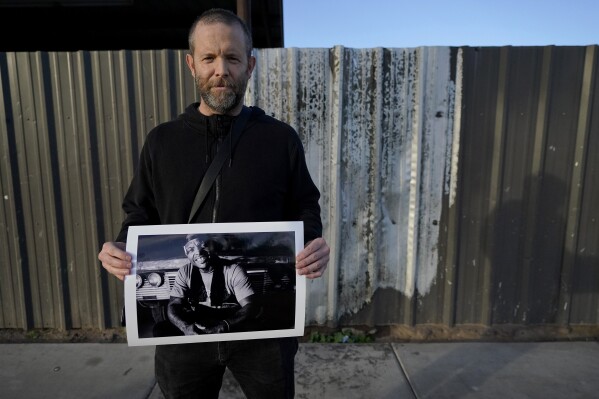 Documentary photographer Eric Elmore displays one of his images of Roosevelt White III, Tuesday, Dec 19, 2023, in Phoenix at the site of a fire where Roosevelt lived in his tent. Elmore documented Phoenix's homeless people in addition to Roosevelt, who was 36 when he died of a stroke in September after falling ill in the Phoenix homeless encampment known as "The Zone". Roosevelt is among thousands of homeless people who died this year and are being remembered at winter solstice events for Homeless Persons' Memorial Day. (AP Photo/Matt York)