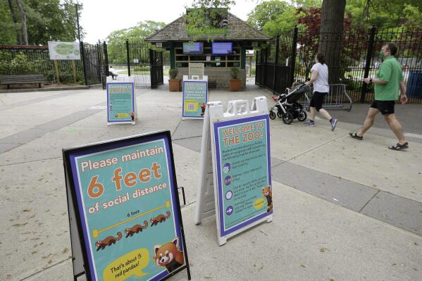 Visitors to the Franklin Park Zoo walk past the signs advising safe distancing near an entrance to the zoo, May 28, 2020, in Boston. A Worcester man has been arrested, Monday, Feb. 21, 2022 for trying to enter a tiger enclosure after breaking into Boston’s Franklin Park Zoo. When questioned by Massachusetts State Police, the man only said that he was very interested in tigers. (AP Photo/Steven Senne, file)