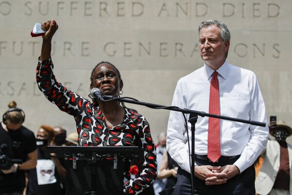 FILE - In this June 4, 2020, file photo, Chirlane McCray, left, wife of New York City Mayor Bill de Blasio, right, raises her fist in solidarity while speaking during a memorial service for George Floyd at Cadman Plaza Park in the Brooklyn borough of New York. Mental health workers will replace police officers in responding to some 911 calls in a test program next year in New York City, de Blasio announced Tuesday, Nov. 10. McCray said, "This is the first time in our history that health professionals will be the default responders to mental health emergencies." (AP Photo/John Minchillo, File)