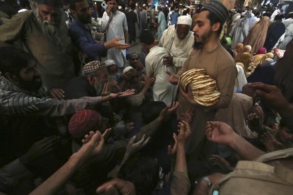 A worker distributes free traditional roti or bread among needy people at a restaurant, in Peshawar, Pakistan, Sunday, April 16, 2023. People are suffering from recent price hike in food, gas, fuel, and power in Pakistan. (AP Photo/Muhammad Sajjad)