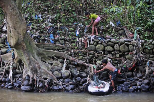 Syachfa Nasution, 12, top, and Adrian Cannavaro, 13, collect plastic trash during a river clean up at polluted Babura River in medan, North Sumatra, Indonesia, Nov. 20, 2021. (AP Photo/Binsar Bakkara)