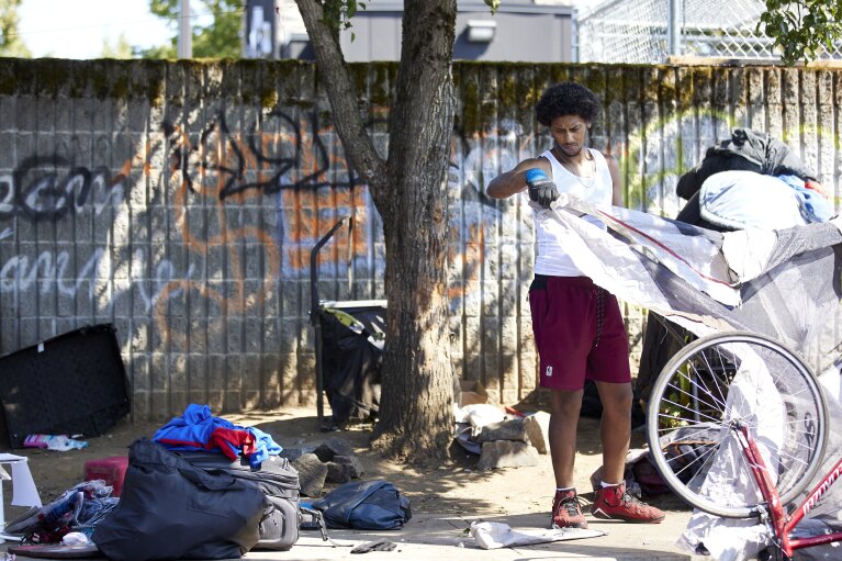 Will Taylor, 32, cleans up the campsite of a friend before Rapid Response Bio Cleanup removes the belongings during a sweep in Portland, Ore., Thursday, July 27, 2023. (AP Photo/Craig Mitchelldyer)