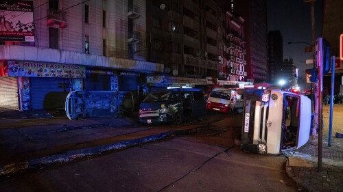 Minibus taxis lie on their side after being blown at the scene of a gas explosion downtown Johannesburg, South Africa, Wednesday July 19, 2023. Search and rescue officials also ordered residents in nearby buildings to evacuate the area and the area where the explosion happened was cordoned off. (AP Photo/Shiraaz Mohamed)