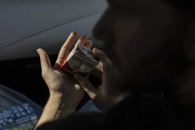 Tyler Baker packs his cigarettes as he talks with his peer support worker Jesse Johnson of the Family Resource Center after she drove him to take a random drug test at the Hancock County Adult Probation office in Findlay, Ohio, Thursday, Oct. 12, 2023. (AP Photo/Carolyn Kaster)