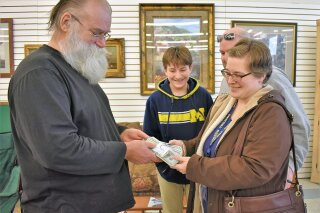 In this Jan. 16, 2020 photo, Howard Kirby, left, gives $43,170 to Kim Fauth-Newberry at a resale store in Owosso Township, Mich.. Kirby's daughter-in-law found the money in a footstool that was don...