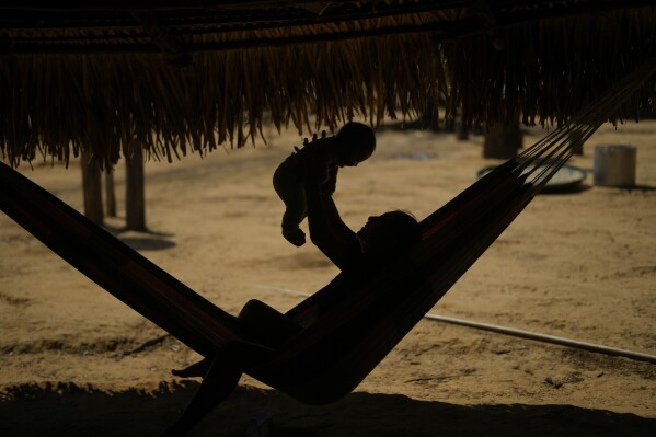 An Indigenous Juma youth holds a baby in a hammock in her community, near Canutama, Amazonas state, Brazil, Sunday, July 9, 2023. The Juma seemed destined to disappear following the death of the last remaining elderly man, but under his three daughters’ leadership, they changed the patriarchal tradition and now fight to preserve their territory and culture. (AP Photo/Andre Penner)