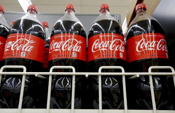 FILE- In this Aug. 8, 2018, file photo bottles of Coca-Cola sit on a shelf in a market in Pittsburgh.  The Coca-Cola Co. said on Thursday, Oct. 22, 2020, it saw gradual improvement in the third quarter, as it turned its focus to emerging leaner from the global pandemic. Atlanta-based Coke said its revenue fell 9% to $8.7 billion.  (AP Photo/Gene J. Puskar, File)