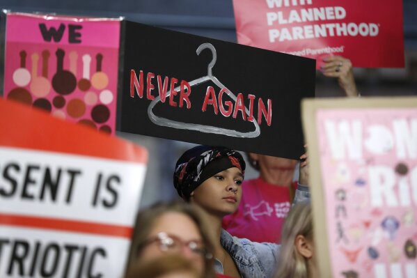 FILE - In this Tuesday, May 21, 2019 file photo, August Mulvihill, of Norwalk, Iowa, center, holds a sign depicting a wire hanger during a rally to protest recent abortion bans put forward in several state legislatures at the Statehouse in Des Moines, Iowa. (AP Photo/Charlie Neibergall)