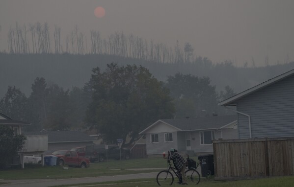 A person rides a bicycle on a smokey day due to wildfires in Fort McMurray, Canada, on Saturday, Sep. 2, 2023. Wildfires are bringing fresh scrutiny to Canada's fossil fuel dominance, its environmentally friendly image and the viability of becoming carbon neutral by 2050. (AP Photo/Victor R. Caivano)