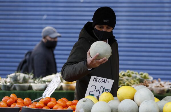 People look for fruit at a market stall in Ilford, London, Friday, Jan. 29, 2021. The borough of Redbridge had the nation's second worst infection rate in January, with an estimated 1 in 15 residents thought to be infected. Officials say the area's ethnic diversity, high levels of poverty and large number of workers in public-facing jobs combine to make it more vulnerable. (AP Photo/Frank Augstein)