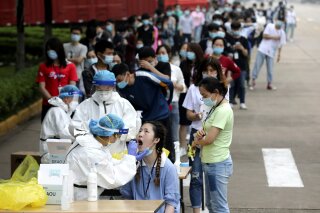 FILE - In this May 15, 2020 file photo, people line up for medical workers to take swabs for the coronavirus test at a large factory in Wuhan in central China's Hubei province. The Chinese city of Wuhan has tested nearly 10-million people for the new coronavirus in an unprecedented 19-day campaign to check an entire city. (Chinatopix Via AP)