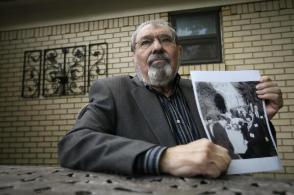 Mike Cochran poses holding a photo Friday, Nov. 15, 2013, at his home in Haltom City, Texas, that shows him and other reporters serving as pallbearers. On a gloomy November afternoon, I helped carry the inexpensive wooden casket of Lee Harvey Oswald to a grave on a slight rise dotted with dying grass. (AP Photo/Tony Gutierrez)