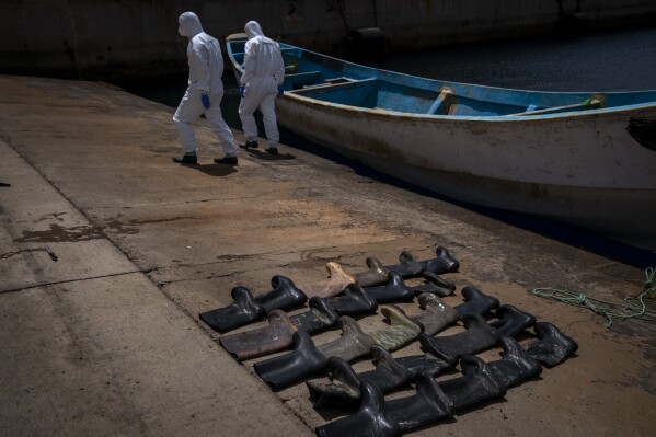 FILE - Rain boots are placed on the ground by police officers as they inspect a boat where 15 Malians were found dead adrift in the Atlantic on Thursday, Aug. 20, 2020, in Gran Canaria island, Spain. The UN migration agency marks a decade since the launch of the Missing Migrants Project, documenting more than 63,000 deaths around the world. More than two-thirds of victims remain unidentified highlighting the size of the crisis and the suffering of families who rarely receive definitive answers. (AP Photo/Emilio Morenatti, File)