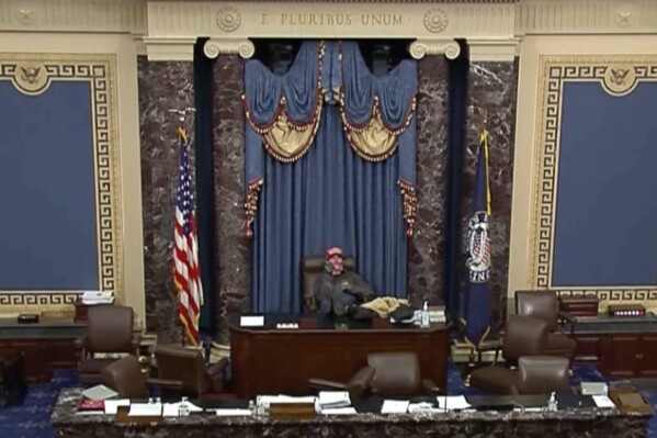 This image from U.S. Senate video, introduced at the trial of Bruno Joseph Cua, shows Cua sitting with his feet up in the Senate chamber on Jan. 6, 2021, during the riot at the U.S. Capitol. Cua, who stormed the U.S. Capitol, assaulted a police officer and sat in a Senate floor chair reserved for the vice president was sentenced on Wednesday, July 26, 2023, to one year in prison.(Senate Television via AP)