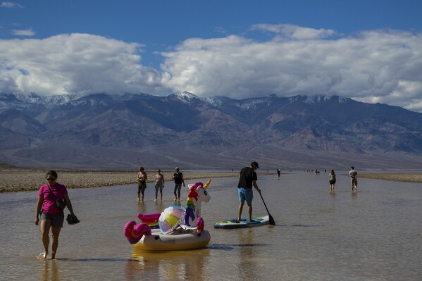 A paddle boarder tows an inflatable unicorn on a temporary lake in Death Valley on Thursday, Feb. 23, 2024, in Death Valley National Park, Calif. A series of storms have brought more than double the parks annual rainfall in the past six months. (AP Photo/Ty ONeil)