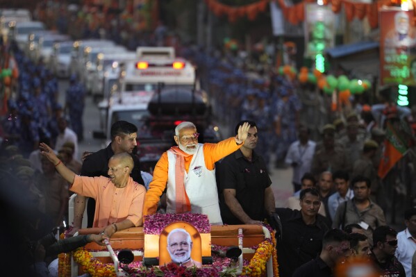 Indian Prime Minister Narendra Modi, in a white waistcoat, and Yogi Adityanath, Chief Minister of Uttar Pradesh greet supporters from a vehicle during a roadshow in Varanasi, India, Monday, May 13, 2024. (AP Photo/Rajesh Kumar)