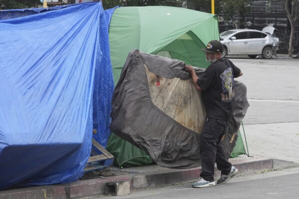 A man carries a mattress into a tent set up on a sidewalk, Monday, May 12, 2025, in Los Angeles. (AP Photo/Damian Dovarganes)