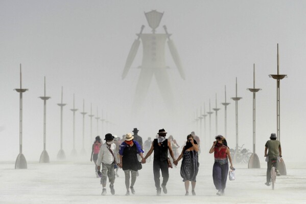 FILE - Burning Man participants walk through dust at the annual Burning Man event on the Black Rock Desert of Gerlach, Nev., on Friday, Aug. 29, 2014. Burning Man organizers don't foresee major changes in 2024 thanks to a hard-won passing grade for cleaning up this year's festival. Some feared their pledge to "leave no trace" might be too tall of a task after a rainstorm turned the desert into a muddy quagmire, temporarily delaying the departure of some 80,000 revelers over the Labor Day holiday. Some question whether it has veered too far from its core principles of radical inclusion and participation. (Andy Barron/The Reno Gazette-Journal via AP, File)