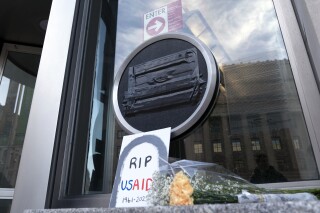 Flowers and a sign are placed outside the headquarters of the U.S. Agency for International Development, or USAID, Feb. 7, 2025, in Washington. (AP Photo/Jose Luis Magana, file)