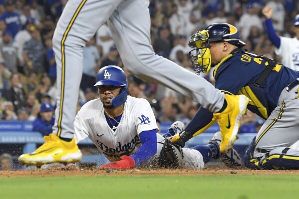 Los Angeles Dodgers' Mookie Betts, center, scores on a double by Freddie Freeman as Milwaukee Brewers catcher William Contreras, right, puts a late tag on him while relief pitcher Abner Uribe backs up the play during the sixth inning of a baseball game Wednesday, Aug. 16, 2023, in Los Angeles. (AP Photo/Mark J. Terrill)