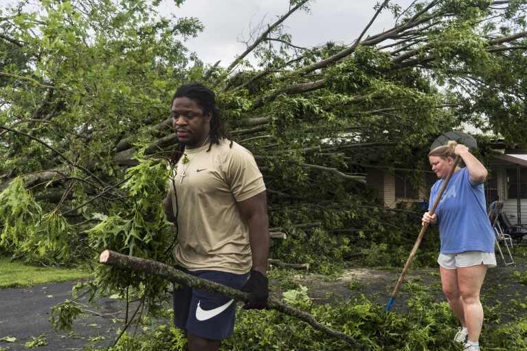 Will Worthey, izquierda, y Lindsey Worthey de Rogers, ayudan a limpiar los escombros de un árbol caído en la casa de Betty Wood en South 24th Street el domingo 26 de mayo de 2024, en Rogers, Arkansas. Poderosas tormentas dejaron un amplio rastro de destrucción en Texas , Oklahoma y Arkansas.  (Charlie Kaijo/The Northwest Arkansas Democrat-Gazette vía AP)